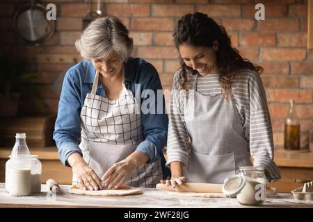 Ältere lateinische Schwiegermutter und Schwiegertochter, die Rollteig kneten Stockfoto