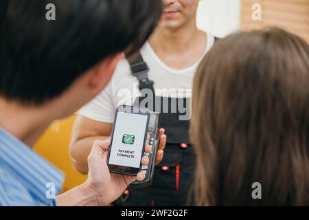 Ein Paar nach dem Umzug scannt QR-Code auf dem Smartphone, um zu bezahlen. Mitarbeiter hält ein Feld. Professionelle Umsteiger sorgen dafür Stockfoto