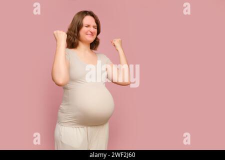 Eine erfolgreiche schwangere Frau auf einem rosa Atelierhintergrund. Schwangerschaft bei einer zufriedenen Frau mit Bauch, Kopierraum Stockfoto