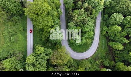 Rotes Auto auf Serpentinenstraße durch grüne Landschaft, Drohnenaufnahme, Oberbayern, Bayern, Deutschland Stockfoto