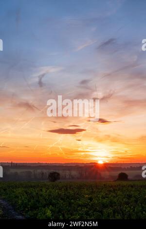 Wintersonnenaufgang über dem kleinen Dorf Chislet, Herne Bay in Kent. Horizont tief im Rahmen mit Ackerland und Feldern. Sonne am Horizont, mit einem überwiegend blauen Himmel mit einigen verstreuten dünnen Wolken. Stockfoto