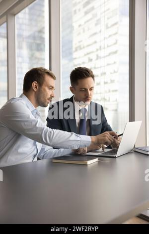 Zwei ernsthafte Geschäftsleute arbeiten am Laptop, sitzen am Arbeitstisch Stockfoto