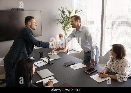 Zwei positive, selbstbewusste Männer schütteln die Hand über den Verhandlungstisch Stockfoto