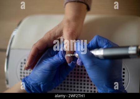 Nahaufnahme eines nicht erkennbaren Nageltechnikers, der beim Entfernen des Deckgels den Nagel eines älteren Kunden feilt Stockfoto