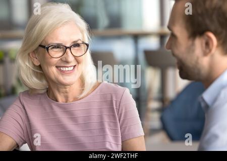 Glückliche attraktive Geschäftsfrau, die mit jüngeren Kollegen spricht Stockfoto