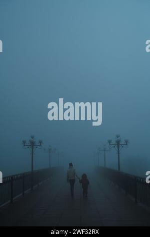 Mystische Silhouetten Rücken einer Frau mit Kind auf einer nebeligen Brücke am Abend im Herbst im Nebelnebel Stockfoto