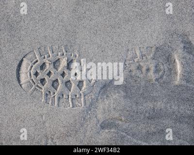 Dieses Bild zeigt den detaillierten Aufdruck einer Wanderschuhsohle auf einem feinen Sandweg, während das Abendlicht ein sanftes Leuchten ausstrahlt. Stockfoto