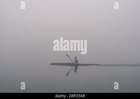 Grado, Italien - 28. Januar 2024: Mädchen übt Rudern während eines Tages dicken Nebels im Grado-Meer. Intensiver Sport mit Kanu/Kajak. Stockfoto