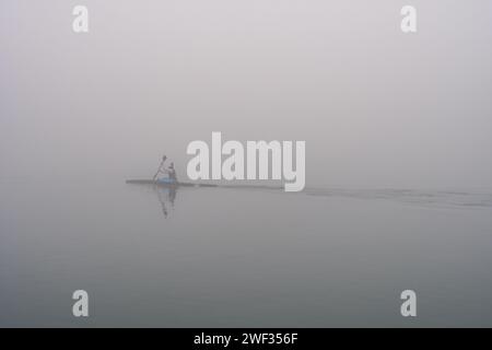 Grado, Italien - 28. Januar 2024: Mädchen übt Rudern während eines Tages dicken Nebels im Grado-Meer. Intensiver Sport mit Kanu/Kajak. Stockfoto