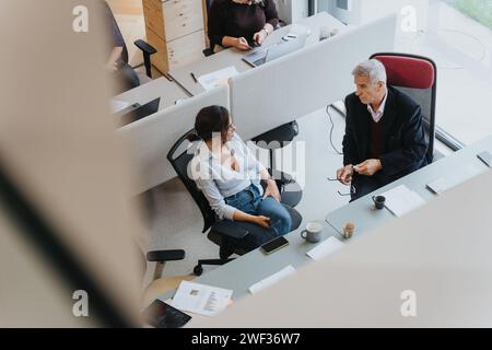 Senior-Geschäftsmann und junge Kollegin in einem modernen Büroumfeld mit einem Gespräch. Stockfoto