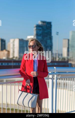 Eine Person in professioneller Kleidung steht selbstbewusst vor dem Hintergrund moderner Stadtarchitektur und verkörpert das Wesen von urbaner Eleganz und sophist Stockfoto