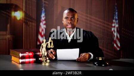 Männlicher Richter Liest Dokumente, Während Er Am Schreibtisch Im Gerichtssaal Sitzt Stockfoto