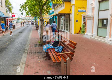 Eine Afrikanerin, die friedlich auf einer Bank schläft, umgeben von Menschen und Touristen, die durch Willemstads zentrale Straße schlendern. Willemstad. Curacao. Stockfoto