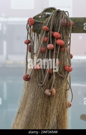 Eine Reihe von Fischernetzen hing in der Nähe des Hafens in der Nähe von Fischerbooten nach einem Angelausflug. Netze, verbunden mit Kunststoffseilen und Schwimmern in verschiedenen Farben Stockfoto