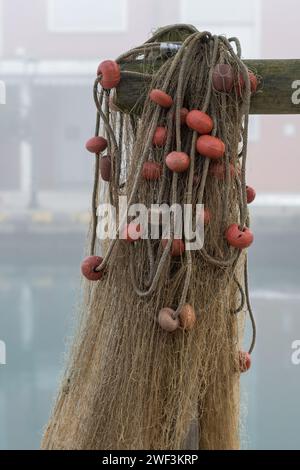 Eine Reihe von Fischernetzen hing in der Nähe des Hafens in der Nähe von Fischerbooten nach einem Angelausflug. Netze, verbunden mit Kunststoffseilen und Schwimmern in verschiedenen Farben Stockfoto