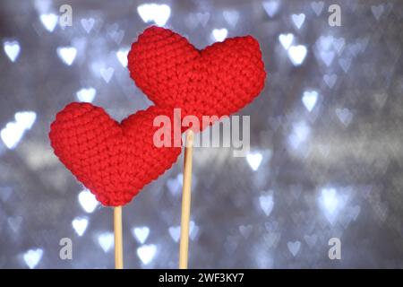 Valentinstag-Konzeptidee. Zwei gestrickte rote Herzen. Herzförmiges Bokeh auf Hintergrund. Selektiver Fokus. Stockfoto