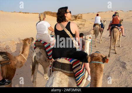 06.11.23 Sahara, Tunesien: Gruppe von Touristen auf Kamelen bei Sonnenuntergang in der Sahara-Wüste Tunesien. Stockfoto