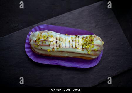 Schließen Sie den köstlichen Eclair-Kuchen - Pistazien aromatisiert mit Sahne und gehackten Nüssen, auf schwarzem Hintergrund. Stockfoto