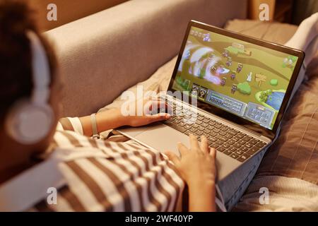 Nahaufnahme eines nicht erkennbaren Teenagers, der Online-Videospiele über Laptop spielt, während er nachts auf dem Bett liegt Stockfoto