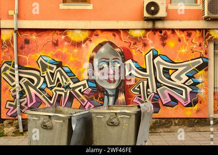 Straßenszene mit Mülltonnen und Graffiti-Girl face Street Art Wandgemälde in Sofia, Bulgarien, Osteuropa, Balkan, EU Stockfoto