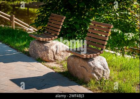 Ursprüngliches Design-Infrastrukturobjekt im Stadtpark. Holzbänke auf großen Steinen. Ein Fußgängerweg führt durch den Park. Smiltene Old Park, L Stockfoto