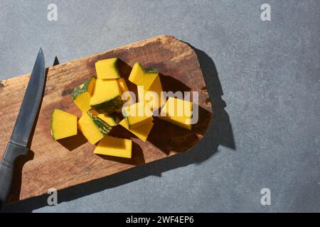 Kürbisscheiben auf einem hölzernen Schneidebrett, in Scheiben geschnittene und Gemüsestücke beim Kochen auf einem Küchentisch mit einem Messer, direkt von oben genommen Stockfoto