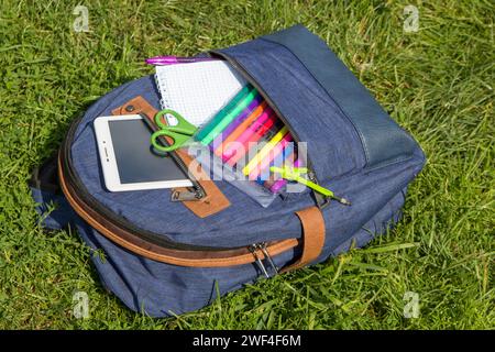 Blauer Rucksack mit Schulaccessoires zum Liegen auf dem Gras Stockfoto