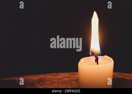 Eine Kerze brennt auf dunklem Hintergrund. Vergrößertes Bild einer Kerze im Dunkeln. Es brennt und symbolisiert Trauer und Trauer. Hintergrund mit Kopierraum Stockfoto