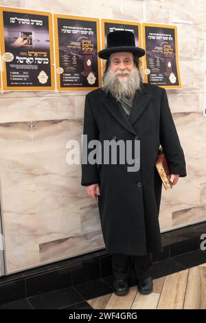 Ein älterer orthodoxer jüdischer Mann posiert für ein Fotobuch über Talmud und vor jiddischen Plakaten. In Brooklyn, New York. Stockfoto