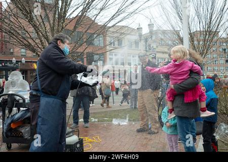 Nach der Fertigstellung seines Eisstücks (links) feuert der Eisbildhauer Jimmy Chiappa ein sehr glückliches junges Mädchen mit Spänen an. Im Columbus Park in Stamford, Connecticut. Stockfoto