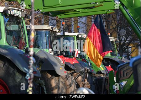 Magdeburg, Deutschland. Januar 2024. Eine deutsche Flagge fliegt zwischen geparkten Traktoren bei der Rallye auf dem Domplatz. Unter dem Motto "zu viel ist zu viel" protestierten Hunderte von Bauern und Forstwirten aus mehreren bundesländern gegen die Haushaltspolitik der Bundesregierung. Quelle: Heiko Rebsch/dpa/Alamy Live News Stockfoto