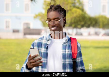 Afrikanischer Student mit Smartphone, blättert draußen durch die Bildungs-App Stockfoto