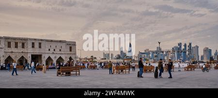 Souq Waqif Doha, Qatar Hauptstraße Sonnenuntergang, zeigt Einheimische und Besucher, die mit der Skyline von Doha im Hintergrund spazieren gehen Stockfoto