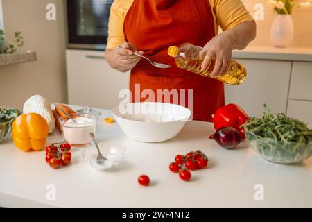 Weibliche Chefin in einer Uniform gießt Olivenöl aus einer Flasche. Kaukasische Bloggerin, die erklärt, wie man ein Gericht kocht Stockfoto