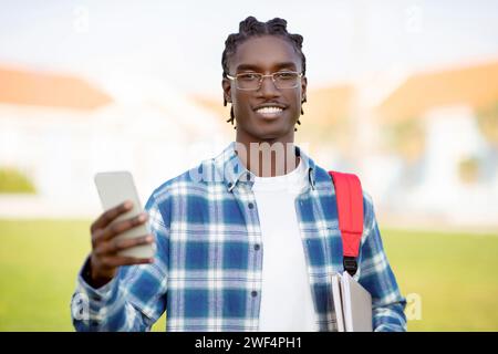 Afroamerikaner Student Guy blättert durch Nachrichten auf Smartphone draußen Stockfoto