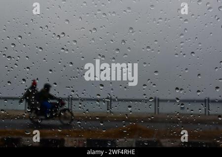 Srinagar, Indien. Januar 2024. Ein Motorradfahrer, der die Straße entlang fährt, wird durch die Windschutzscheibe des Autos gesehen, die bei leichtem Regen mit Regentropfen übersät ist. Kaschmirs Berge waren leicht schneebedeckt und die Ebenen erlebten am Sonntag leichte Regenfälle, die die lange Trockenzeit der letzten zwei Monate brachen. (Foto: Saqib Majeed/SOPA Images/SIPA USA) Credit: SIPA USA/Alamy Live News Stockfoto