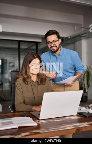 Glücklicher junger Manager, der reiferen Angestellten hilft, Computerarbeit zu erklären. Stockfoto
