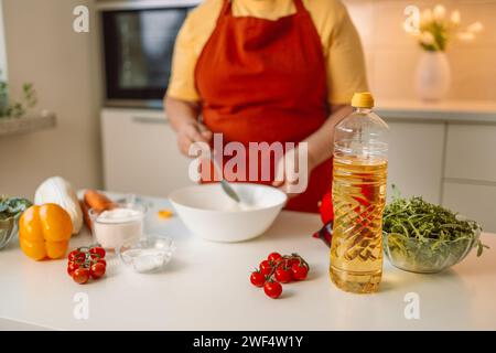 Weibliche Chefin in einer Uniform gießt Olivenöl aus einer Flasche. Kaukasische Bloggerin, die erklärt, wie man ein Gericht kocht Stockfoto