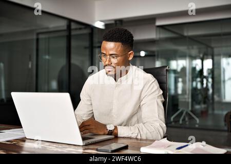 Beschäftigter männlicher afrikanischer Firmenangestellter, der im Büro mit einem Laptop arbeitet. Stockfoto