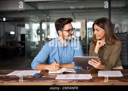 Fröhliche, beschäftigte lateinamerikanische Partner, die im Büro mit einem digitalen Tablet arbeiten. Stockfoto