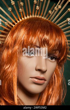 Rothaarige Plastikpuppe mit hellen, langen Haaren, die eine goldene Krone trägt, die auf grünem Hintergrund posiert Stockfoto