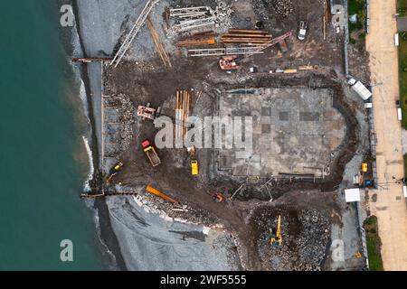 Von oben nach unten auf die Baustelle mit Baggern und Muldenkippern bei Erdarbeiten und Fundamentbauten am Meer Stockfoto