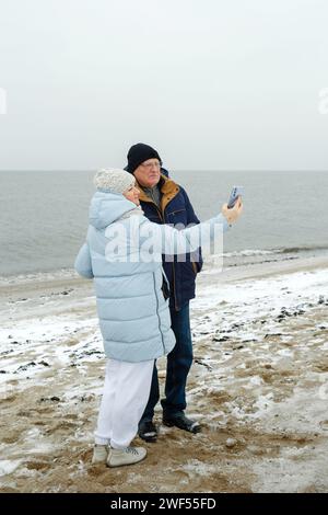 Porträt eines älteren Ehepaares, das einen Winterspaziergang am Strand macht und ein Selfie macht. Vertikaler Rahmen. Stockfoto