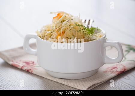 Sauerkraut mit Karotten und Gewürzen in einer weißen Schüssel auf einem hellen Holztisch. Stockfoto