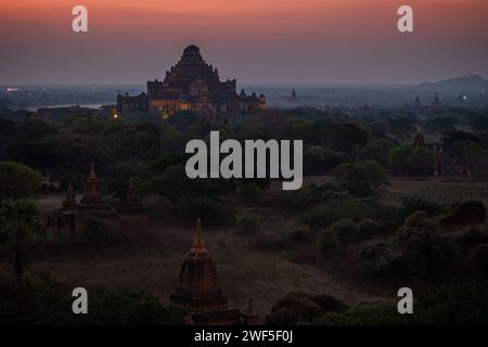 Malerischer Blick auf den beleuchteten Dhammayangyi Tempel und viele andere Tempel und Pagoden in der nebeligen Ebene von Bagan in Myanmar (Burma), in der Abenddämmerung. Stockfoto