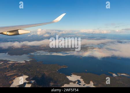 Fliegen über den Wolken. Blick auf den klaren blauen Himmel, den Flugzeugflügel und die Seen und landen an einem sonnigen Tag. Stockfoto