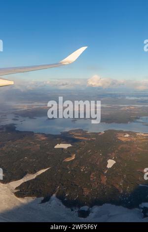 Fliegen über den Wolken. Blick auf den klaren blauen Himmel, den Flugzeugflügel und die Seen und landen an einem sonnigen Tag. Stockfoto