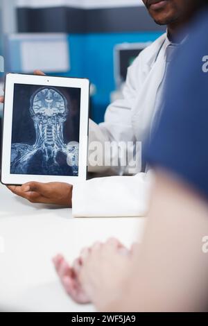 Nahaufnahme des Röntgenergebnisses auf einem digitalen Tablet im Gesundheitswesen. Schwarzer Arzt hält digitales Gerät mit Röntgenaufnahme von Gehirn und Knochen, die mögliche Tumoren oder schwere Krankheiten und Symptome anzeigt. Stockfoto