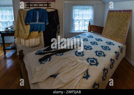 Eine Ausstellung von Möbeln und Kleidern der Leuchtturmwärterin Sarah Lane füllt ein Schlafzimmer im Mission Point Lighthouse auf der Old Mission Peninsula, Traverse City, Peninsula Township, Michigan, Vereinigte Staaten. Nach dem Tod ihres Mannes und Mitwärters, Kapitän John Lane, im Jahr 1906 übernahm die 67-jährige Sarah Lane alle seine Pflichten und wurde die erste und einzige weibliche Wärterin des Leuchtturms. Sie diente insgesamt von 1881 bis 1907 und verdiente 540 Dollar im Jahr – nur die Hälfte dessen, was ihr Mann für dieselbe Arbeit bezahlt worden war. Stockfoto