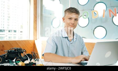 Teenager, der am Laptop arbeitet und in der MINT-Klasse die Kamera ansieht. Kaukasischer Schüler, der Daten beim Suchen analysiert Stockfoto